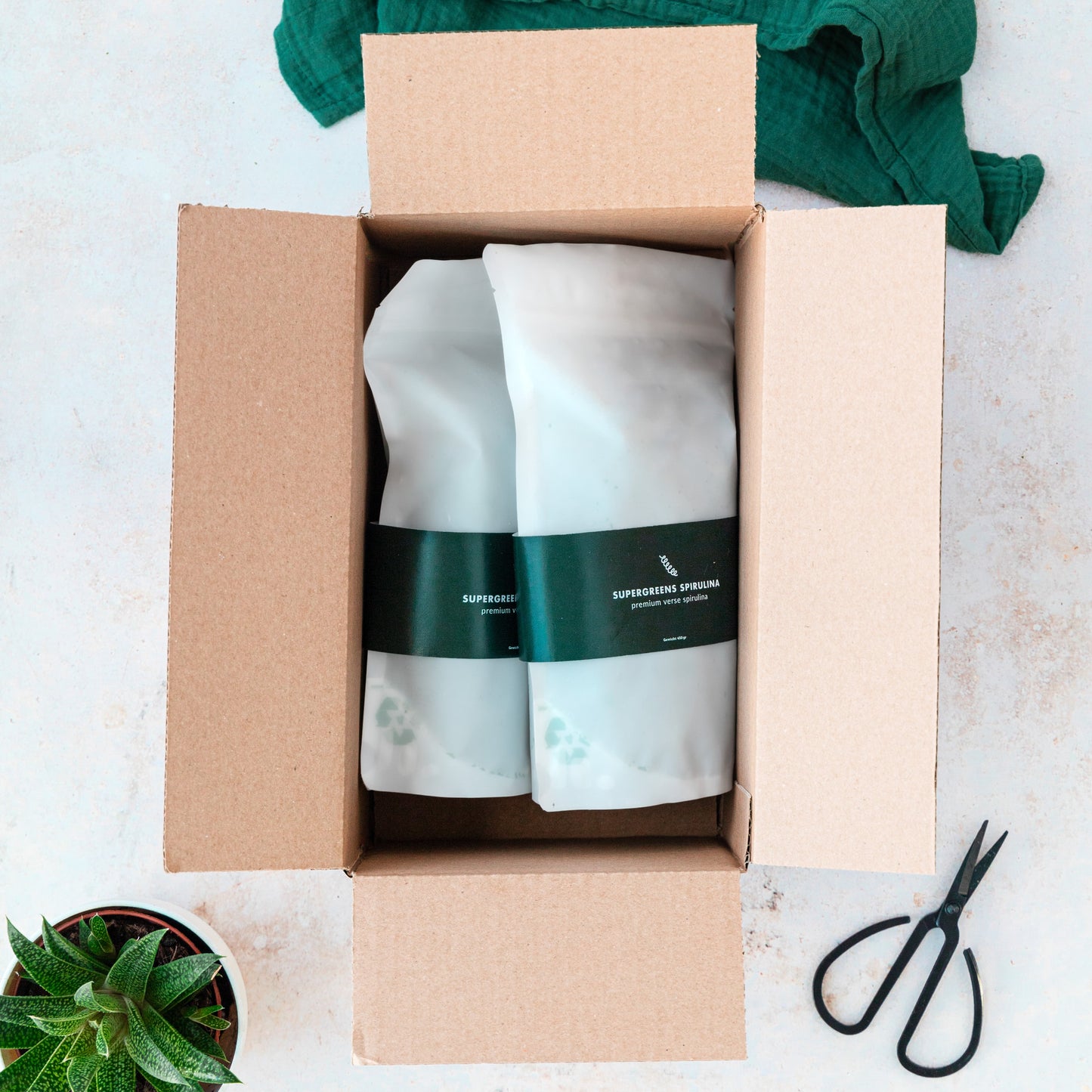 Een kartonnen doos met daarin liggend twee stazakken bevroren spirulina van Supergreens Spirulina